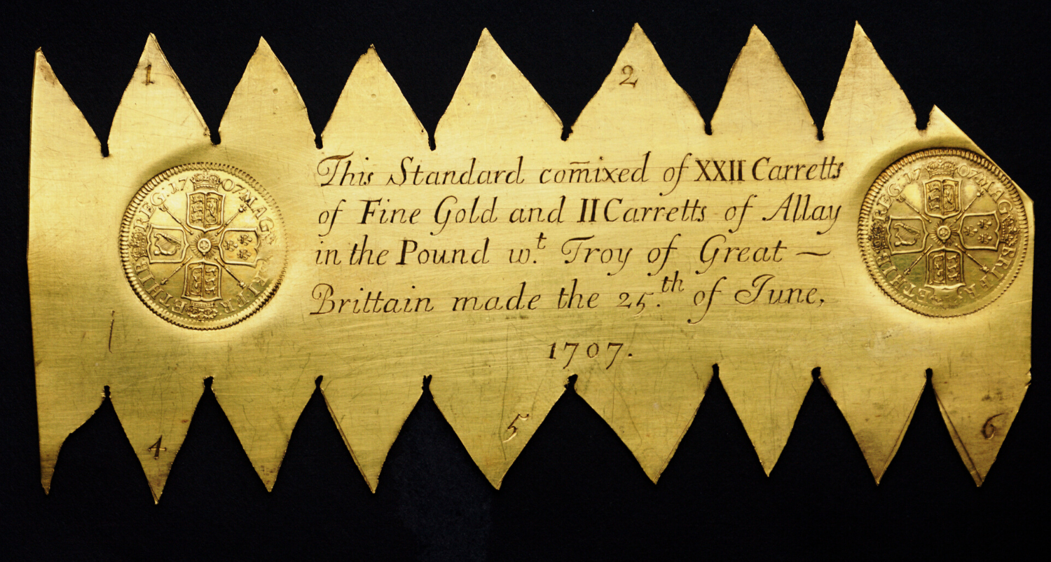 A gold plate with large jagged edges and the impression of a coin pressed into it.