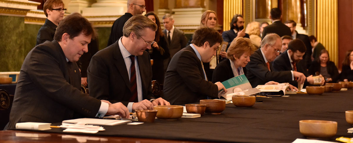 A row of people sitting at a table with bowls in front of them inspecting coins at the historic Trial of the Pyx ceremony.